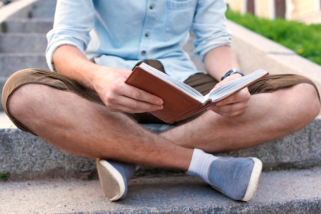 No face. Student with book sit on the stairs in campus