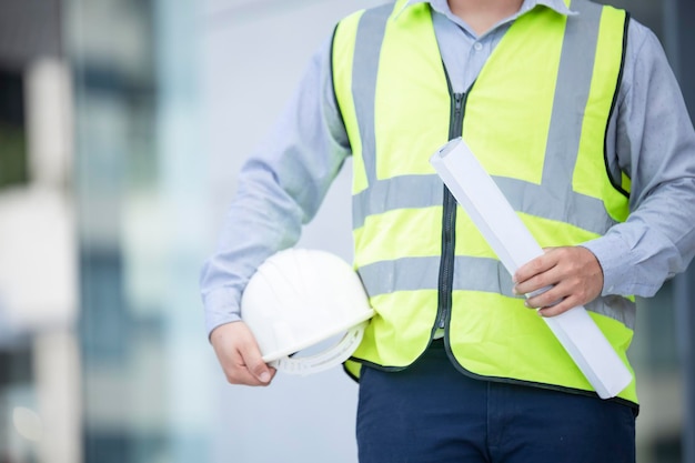 No face unrecognizable person torso engineer worker or architect holding in hand blueprint and white plastic helmet hardhat on blur background empty copy space for inscription objects