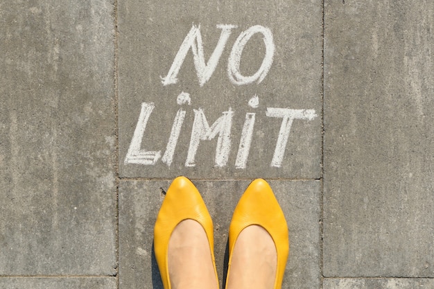 Photo no limit text on gray sidewalk with woman legs, top view