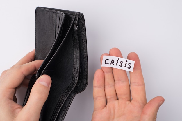 No money and work concept. Cropped close up overhead view photo of male hands holding empty open wallet and word crisis on palm isolated over grey background