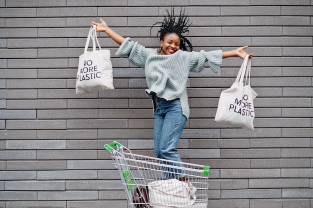 No more plastic. African woman with shopping cart trolley and eco bags jump outdoor market.