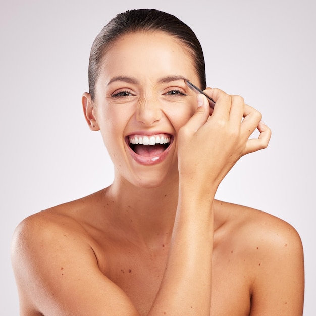 No pain no gain Shot of an attractive young woman plucking her eyebrows against a studio background