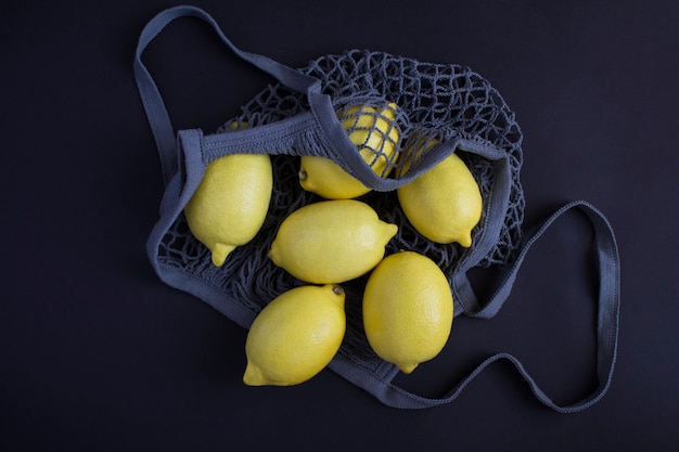 No plastic bag concept. Mesh shopping gray bag with lemon on the black background. Top view. Close-up.