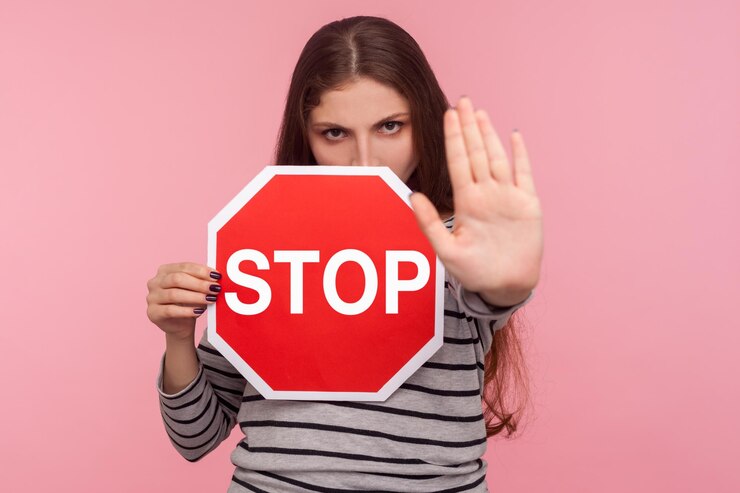 Photo no prohibited portrait of strict bossy girl looking angrily and showing stop gesture holding road traffic sign as warning of ban forbidden access indoor studio shot isolated on pink background