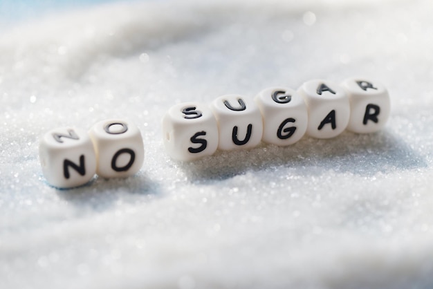 다이어트를 제안하고 건강을 위해 설탕을 덜 먹도록 나무 배경에 흰 설탕이 있는 설탕 텍스트 블록이 없습니다.
