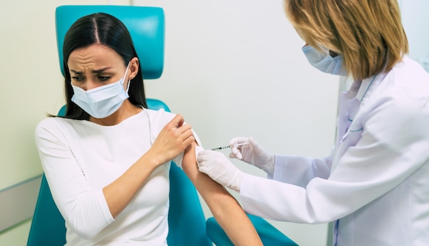 No Vaccination. Scared woman Gesturing Stop To Hand Offering Syringe With Vaccine Refusing To Be Vaccinated. Needle Phobia, Fear Of Covid-19 Vaccines