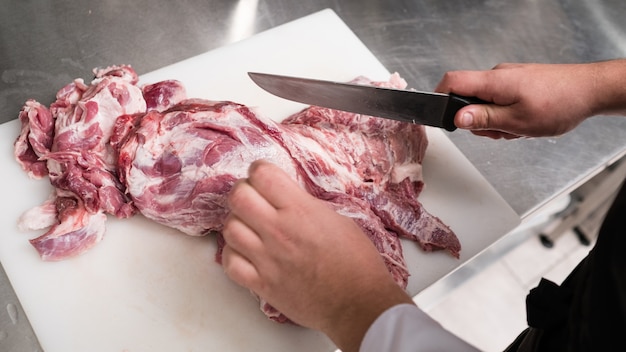 Photo no vegans here. skillful cook in black apron cuts fresh red pork meat in the restaurant kitchen.