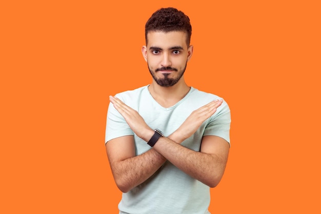 No way absolutely not Portrait of determined brunette man with beard in white tshirt showing x sign with crossed hands meaning stop this is the end studio shot isolated on orange background