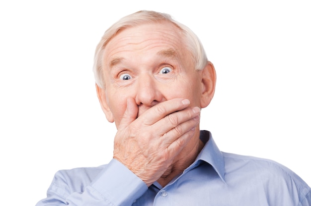 No way! Excited senior man formalwear covering mouth with hand and looking at camera while standing against white background