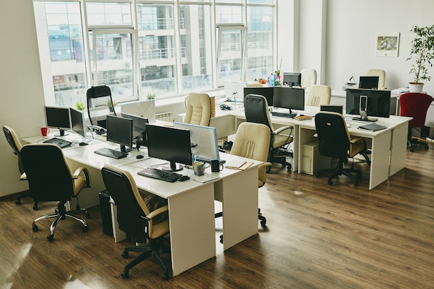 Nobody in modern office with big window and desks with computers and mugs