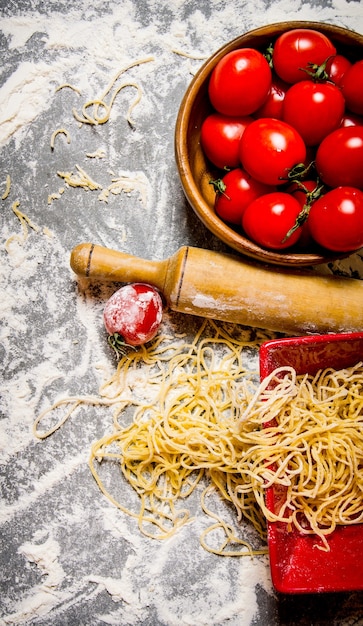 Noedels met tomaten in een kopje en deegroller. Op de stenen tafel met bloem. Bovenaanzicht