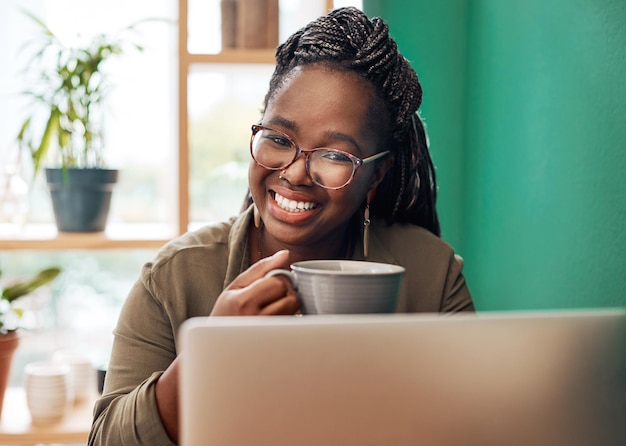 Noem het mijn kleine coffeeshopkantoor Shot van een jonge vrouw die koffie drinkt en een laptop gebruikt in een café