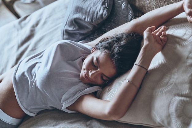 Nog een minuutje in bed? Bovenaanzicht van aantrekkelijke jonge vrouw die de ogen gesloten houdt en glimlacht