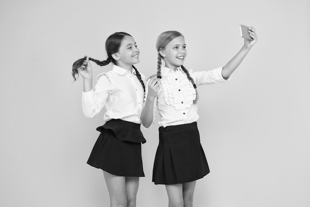 Nog een selfie gelukkige schoolkinderen nemen selfie met smartphone op gele achtergrond kleine meisjes glimlachen naar selfie camera in mobiele telefoon genieten van selfie-sessie op 1 september