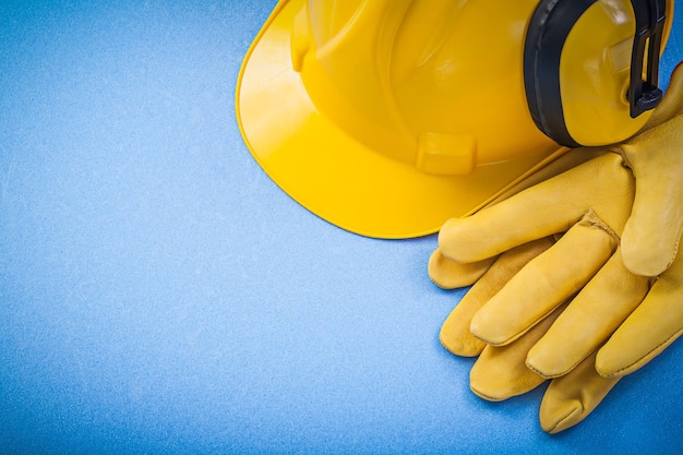 Noise reduction earmuffs protective gloves hard hat on blue background construction concept