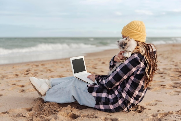 Фото Женщина-кочевник со своей кошкой с помощью ноутбука на пляже концепция путешествий и кочевого образа жизни