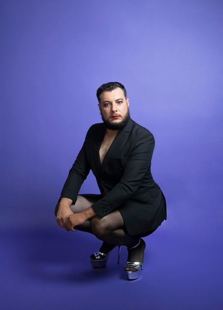 Non binary person sitting wearing elegant clothes in studio on isolated purple background