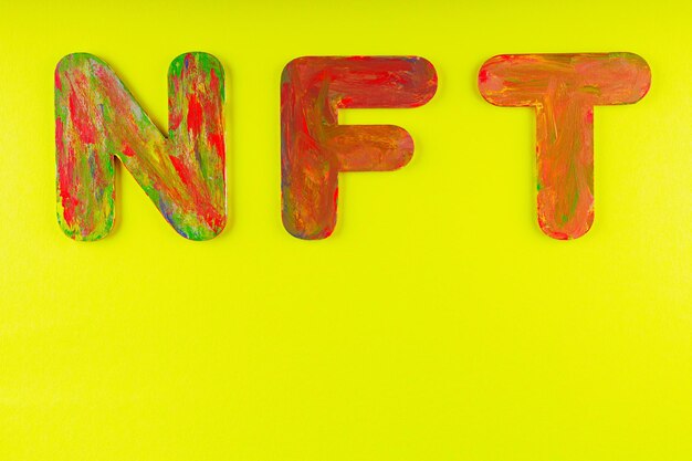 Non fungible token. NFT acronym of multicolored letters on yellow background. Crypto Art concept. Copy space. Top view