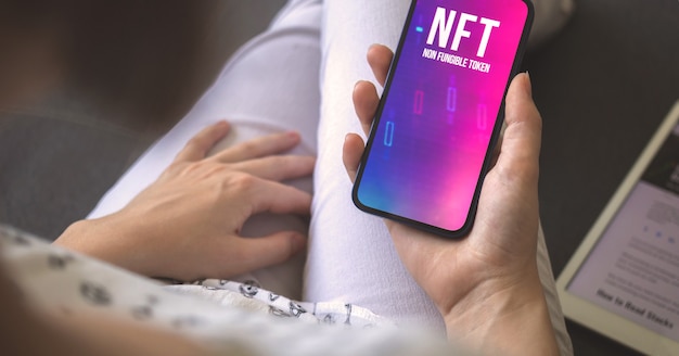 Non-fungible token. Smartphone screen with NFT logo in woman hand. Concept of crypto art and technology photo