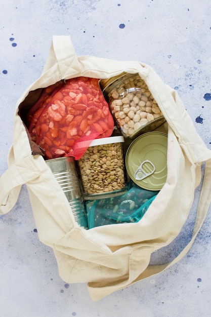 Nonperishable food canned goods in eco cotton bag nuts lentilsbeans chickpea and canned foods on a blue background