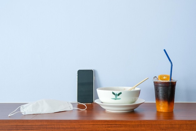 Noodle bowl oranje ijskoffie en gezondheidsmasker op houten tafel