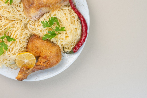 Noodle, chicken meat, pepper and sliced lemon on a plate, on the marble surface