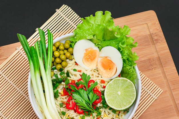 Noodle dish with green onions eggs green pea red hot pepper greens and lime