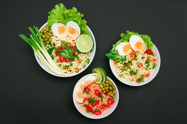 Noodle dish with green onions eggs green pea red hot pepper greens and lime