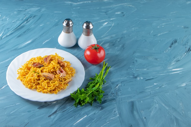 Noodle with meat on a plate next to parsley bunch, tomatoes and salt, on the marble background. 