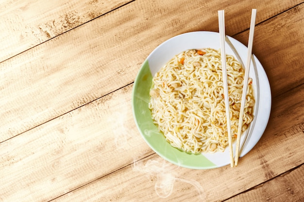 Noodles on the bowl with spoon and fork on wooden table