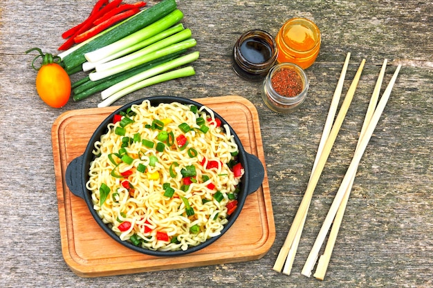 Noodles in Chinese style in a cast-iron frying pan on a wooden stand. Chinese noodles with vegetables and chili peppers. Spicy vegetarian noodles with vegetables.