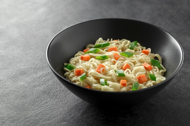 Noodles instant gekookt met groenten wortel en groene ui donkere kom selectieve focus