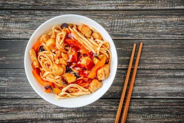 Noodles udon in sweet and sour sauce and chopsticks on wooden table