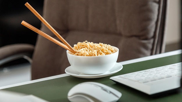 Foto tagliatelle con le bacchette sul posto di lavoro vicino al computer portatile durante la pausa pranzo cibo spazzatura