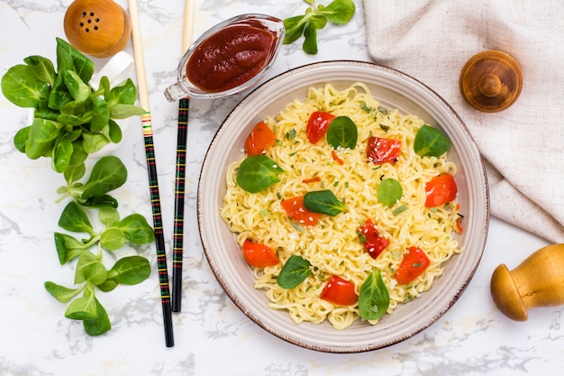 Noodles with pepper, lettuce leaves and sesame seeds in a ceramic plate, top view