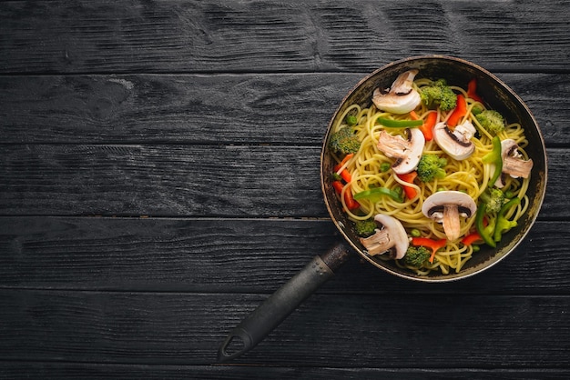 Noodles with vegetables in a frying pan Asian Cuisine Pasta Top view Free space On a wooden background