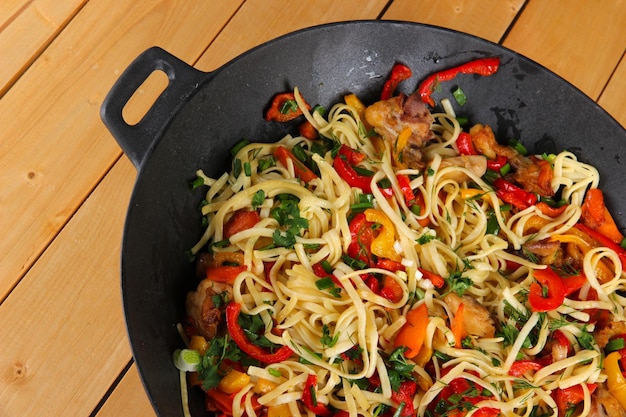 Photo noodles with vegetables on wok on wooden background