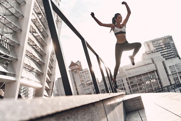 Nooit ophouden! Volledige lengte van moderne jonge vrouw in sportkleding die springt tijdens het sporten buitenshuis