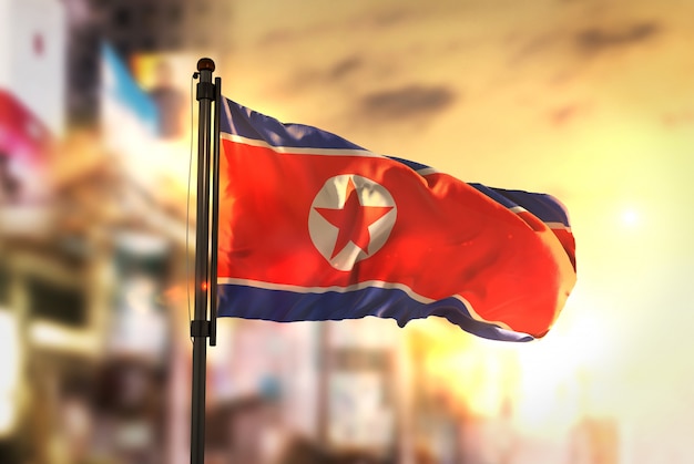 Noord-korea vlag tegen stad wazige achtergrond bij zonsopgang achtergrondverlichting