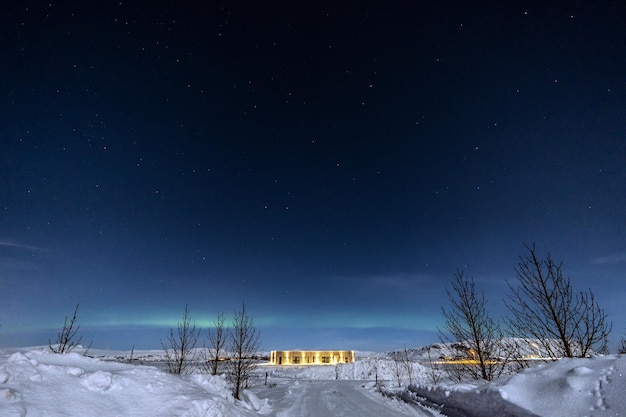 Noorderlicht aan de horizonlijn en sterren met aan het einde een ultramodern verlicht huis