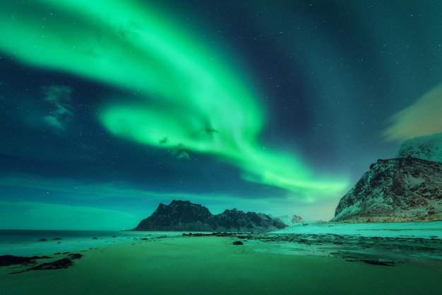 Noorderlicht op de Lofoten-eilanden Noorwegen Groene aurora borealis Sterrenhemel met poollicht Winterlandschap met heldere aurora zee zandstrand en besneeuwde bergen Uttakleiv strand 's nachts