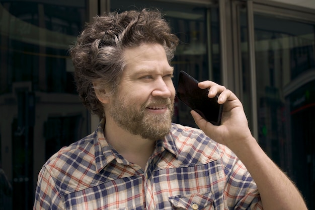 Noordse man met baard en glimlach praten op mobiele telefoon op straat