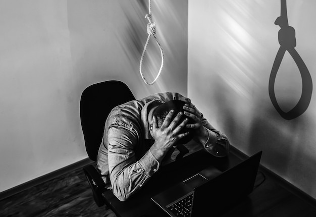Фото Петля над офисным работником. концепция самоубийства. зависание из-за стресса на работе. депрессия эмоционального выгорания. ужасная жизненная ситуация. мужчина возле ноутбука за столом.