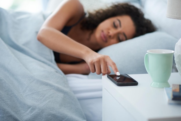 No, ti sto ignorando, signor alarm shot di una giovane donna attraente sdraiata a letto durante la mattina e che preme snooze sul suo telefono