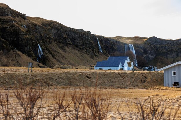 Nordic countryside landscape with lands and fields with cosy cottages near snowy mountains. Amazing picturesque highland scenery with farmhouses, icelandic hills and natural setting.