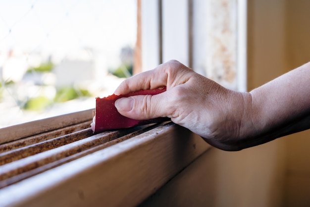 Normal view of a woman's hands with a sandpaper sanding a window frame before painting Empowered woman concept