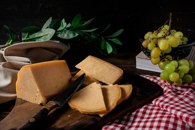 Normale weergave van een stuk provolone kaas gesneden op een bord en wat druiven op de achtergrond.