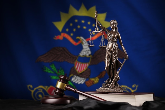 Photo north dakota us state flag with statue of lady justice constitution and judge hammer on black drapery concept of judgement and guilt