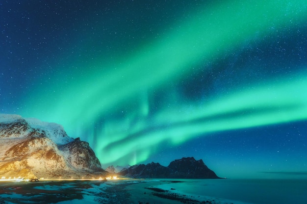 Northern lights in Lofoten islands Norway Green Aurora borealis Starry sky with polar lights Night winter landscape with aurora sea with sky reflection rocks beach and snowy mountains Nature