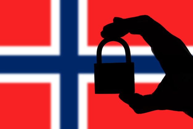 Norway security Silhouette of hand holding a padlock over national flag